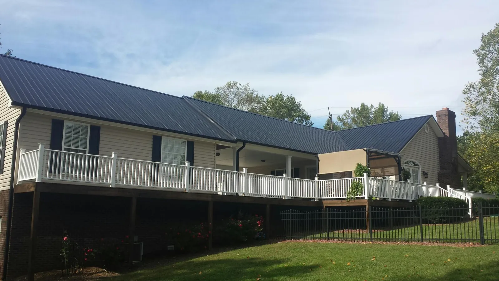 Black metal roof above a long white railed deck on a hillside home in Somerville